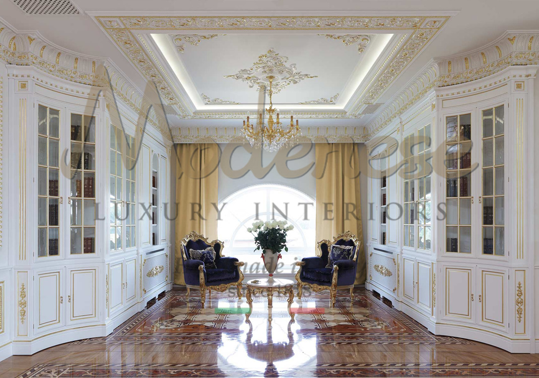 White and gold leaf bookshelves and 2 central blue fabric armchairs with round table and decorative vase Modenese