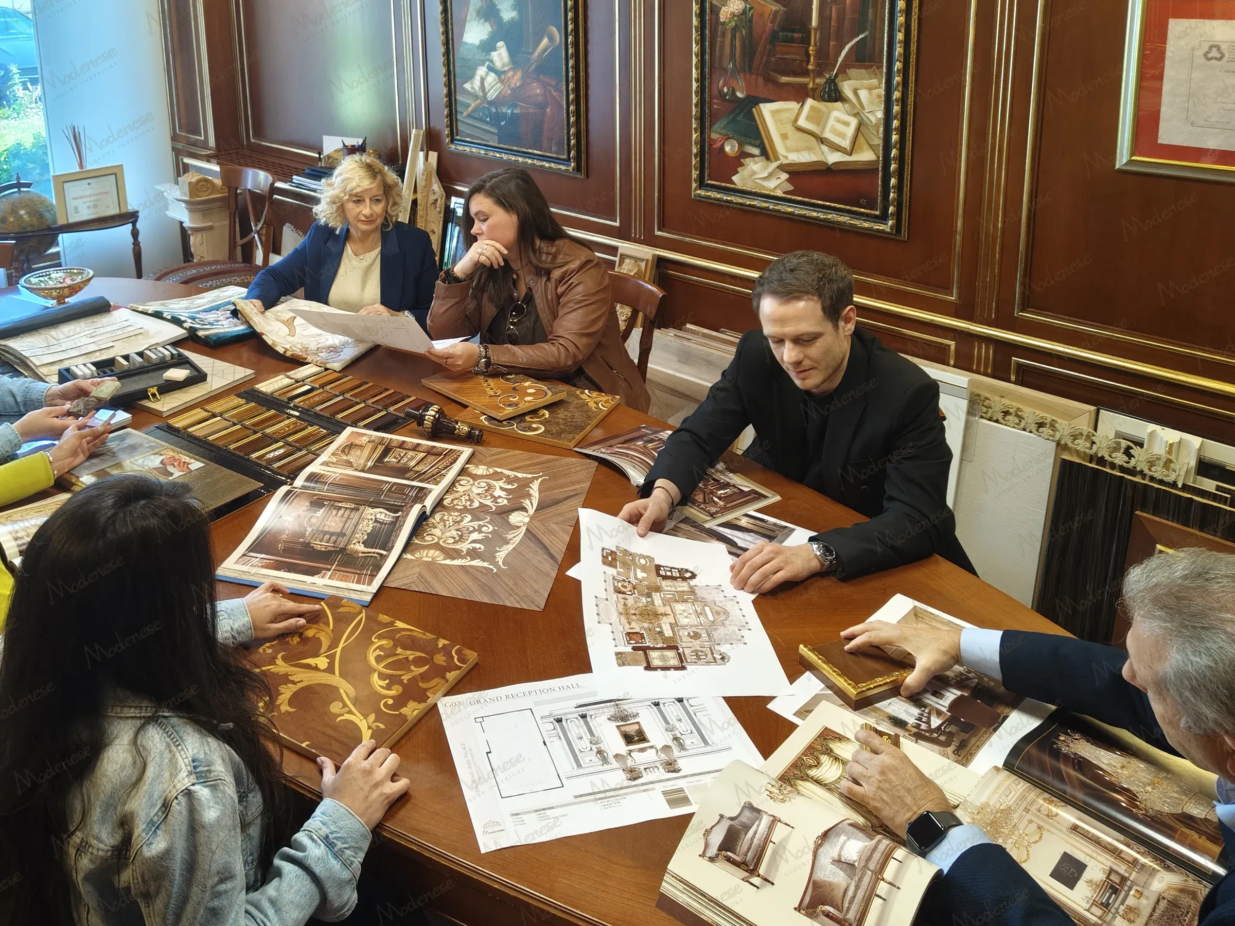 Group of interior designers collaborating over luxury classical design plans and wood inlay samples in a Milan studio office with ornate wall paneling and traditional artwork