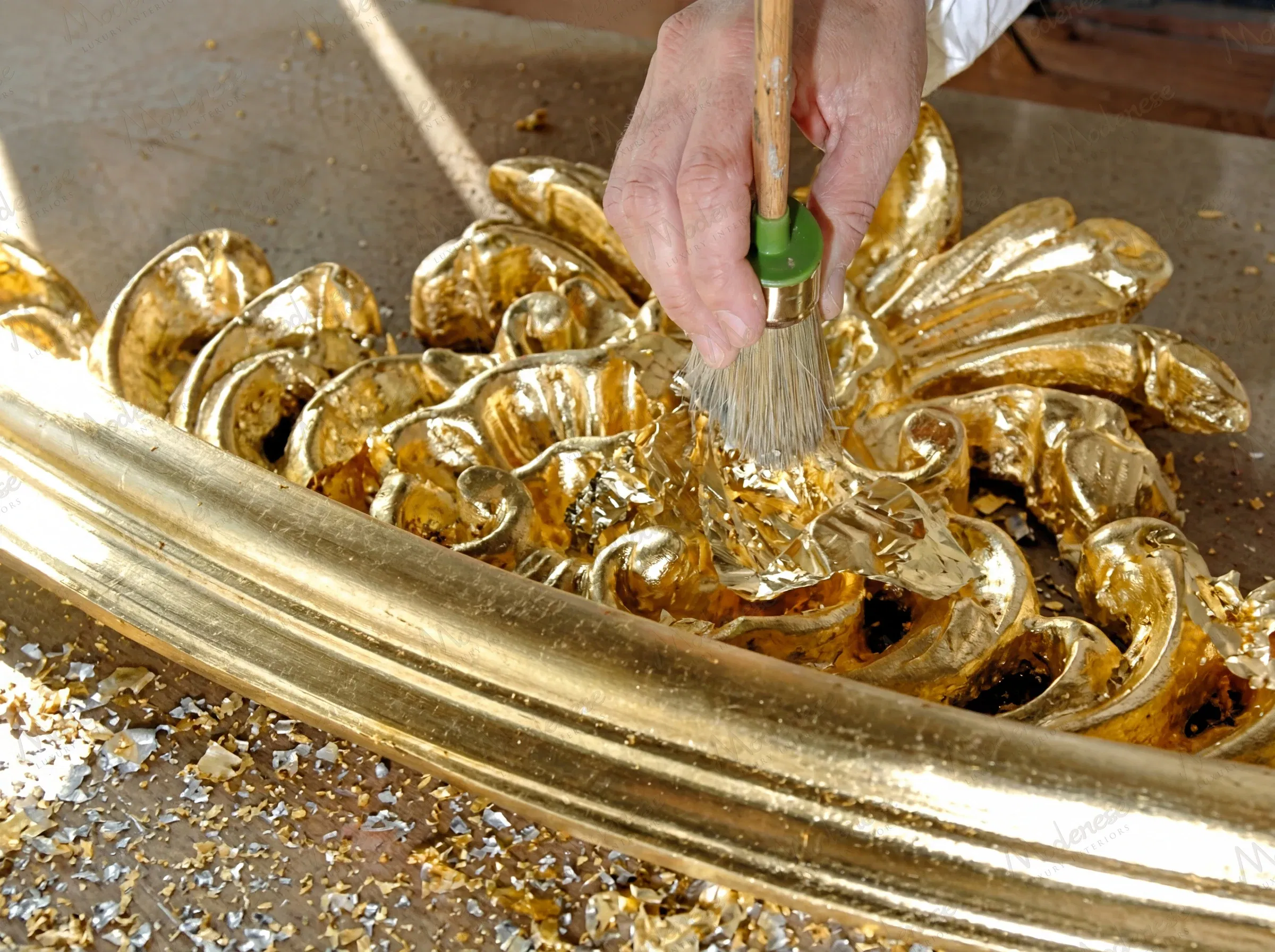 حرفي يطبق أوراق الذهب على عنصر زخرفي متقن أثناء عملية التذهيب في مصنع Modenese Interiors