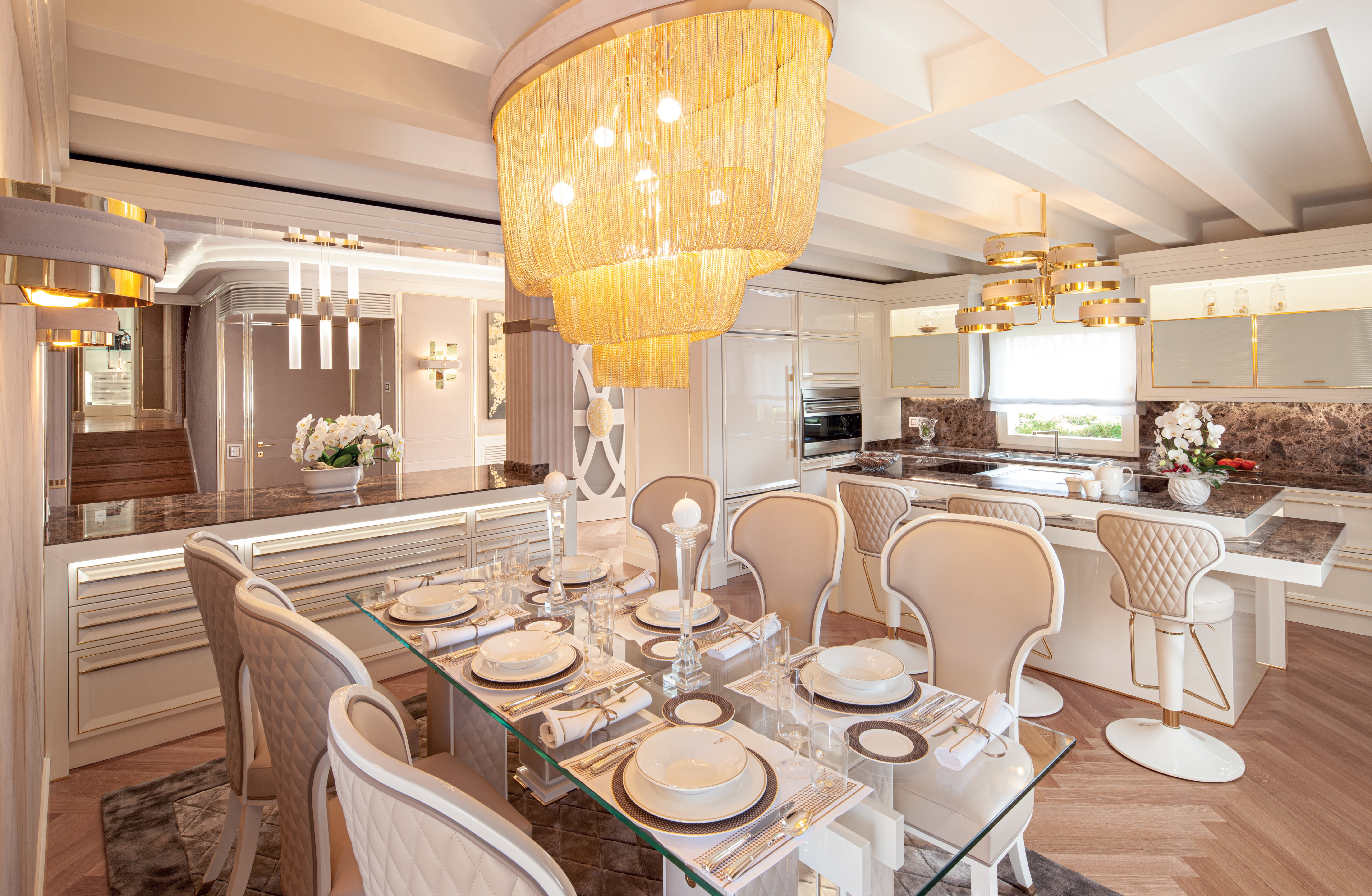 Dining area with glass table, upholstered chairs and statement chandelier next to the Prestige kitchen